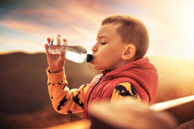 Doğada su içen küçük bir çocuk, sağlık kavramı. Gün batımı..