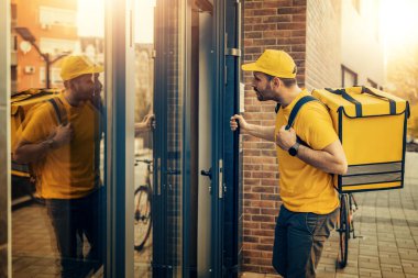 Sırtında teslimat kutusu olan sarı üniformalı bir kurye. Müşterilere yemek dağıtımı. İnternetten alışveriş..
