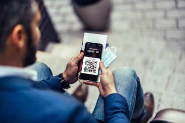 Yeşil pasaportlu cep telefonu taşıyan bir adam, Covid-19 aşısı sertifikası.