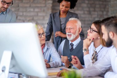 Ofis masasında birlikte otururken çalışan ve iletişim kuran bir grup iş adamı..