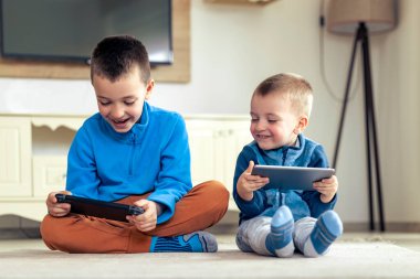 Çocuklar evdeki tablet ve konsolda video oyunu oynuyorlar.