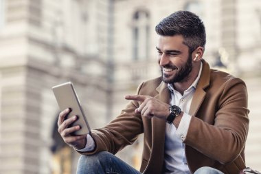Şehir sokaklarında otururken dijital tablet kullanan bir adam. Acil iş. Modern teknoloji kavramı.