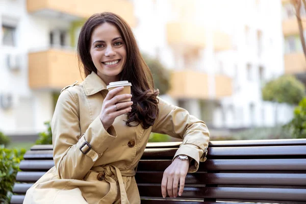 Woman take a break from work and sitting on a bench outside her office while drink coffee to go.