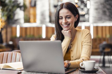 Bir kafede dizüstü bilgisayar kullanan çekici bir genç kadının portresi. Kahve dükkanında dizüstü bilgisayarda çalışan bir kadın..
