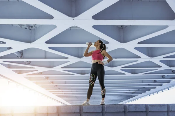 スポーツウェア飲料水の魅力的なフィットネス女性市橋の上でトレーニングした後 — ストック写真