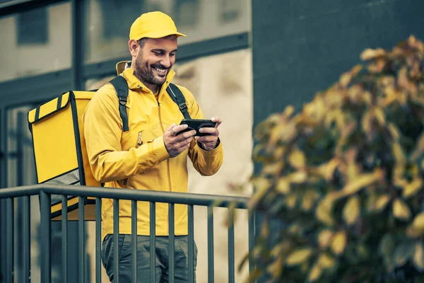 Yemek teslimatı için üniformalı genç bir adam. Akıllı telefon kullanıyor..