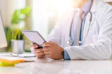 Doktorun ofisinde tablet kullandığı yakın plan, doktor internette çalışıyor..