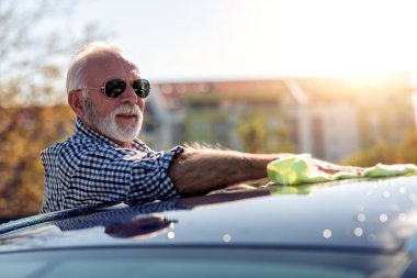 Dışarıda arabasını temizleyen kıdemli bir adam. Mikrofiberli bir adam arabanın cilasını siliyor..