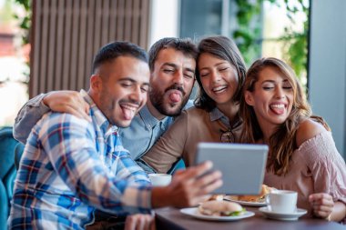 Bir grup arkadaş kafede selfie çekiyorlar. Gülümsüyorlar ve birlikte eğleniyorlar. Arkadaşlar, boş zaman ve mutluluk konsepti..
