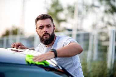 Gün ışığında arabasını temizleyen genç bir adamın portresi..