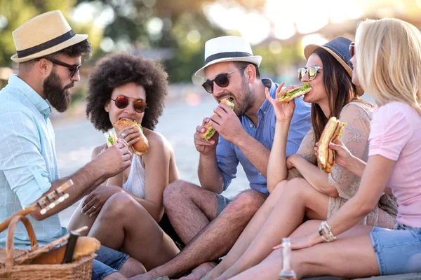 Group of people eating sandwiches during picnic on the beach.