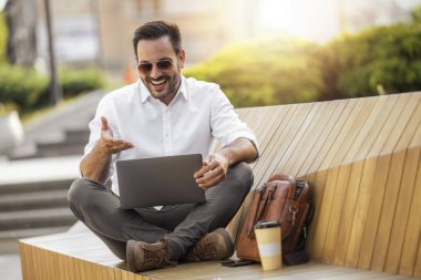 Genç işadamı parkta oturan ve dizüstü bilgisayar kullanarak.