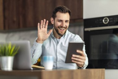 Yakışıklı adam dijital tablet kullanıyor ve evde otururken gülümsüyor..