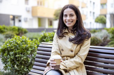 Kadın işe ara veriyor ve kahve içerken ofisinin dışındaki bankta oturuyor. Güneşli bir gün.