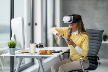 Genç iş kadını ofisinde sanal gerçeklik cihazını kullanıyor. Ofiste eğleniyor ve eğleniyor..