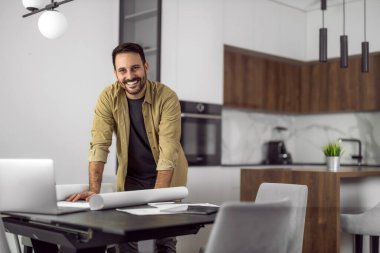 Yeni fikirler üzerinde çalışan erkek tasarımcı. Evde çalışan gülümseyen bir adamın portresi. Kameraya bakıyor..