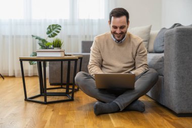 Evde çalışırken dizüstü bilgisayar kullanan genç bir adam. Evde çalışan serbest çalışan bir erkek. Çevrimiçi alışveriş..