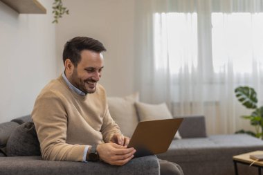 Evde çalışırken dizüstü bilgisayar kullanan genç bir adam. Evde çalışan serbest çalışan bir erkek. Çevrimiçi alışveriş..