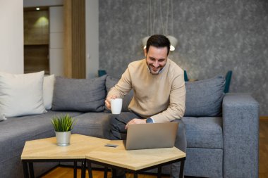 Evde çalışırken dizüstü bilgisayar kullanan genç bir adam. Evde çalışan serbest çalışan bir erkek. Çevrimiçi alışveriş..