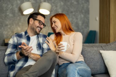 Mutlu genç çift evde otururken kahve içip gülümsüyor. Kahve zamanı..