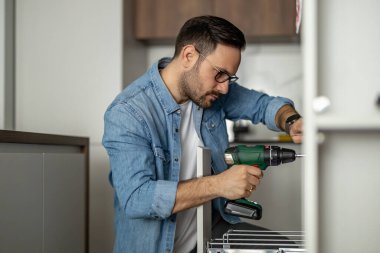 Marangoz mutfak montajını tamamlıyor. Adam mutfağa elektrikli tornavida kullanıyor. İnşaat, bakım ve onarım konsepti..