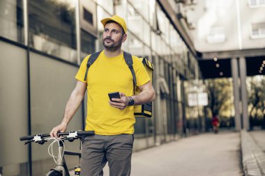 Şehir sokaklarında termal çantalı ve bisikletli mutlu teslimatçı. Müşterilere yemek dağıtıyor..
