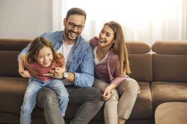 Gülümseyen genç ebeveynler ve kızları evde eğleniyorlar. Hafta sonu evde..