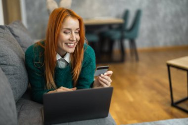 Kanepeye uzanmış, dizüstü bilgisayar kullanan genç bir kadın portresi. İnternetten alışveriş yapan genç bir kadın..