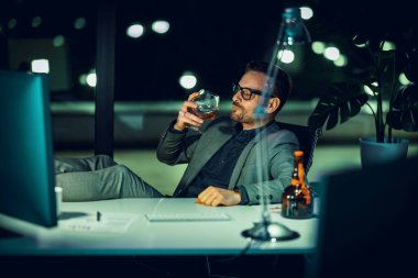 Gecenin geç saatlerinde bilgisayarda çalışan yakışıklı iş adamının portresi. İşadamı gece geç saatlere kadar bilgisayarla ofiste çalışıyor..