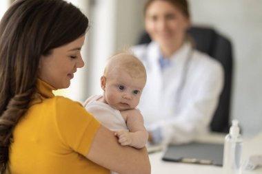 Anne ve şirin bebeği klinikte çocuk doktorunu ziyaret ediyor. Bebek doktoru ve doktor ofisinde bebeği var..