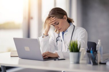 Kadın doktor portresi klinikte online bir hastayla konuşuyor. Yurtiçi sağlık tedavisi için online danışmanlık yapıyor. O, yoğun bir iş gününden sonra baş ağrısı çekiyor..