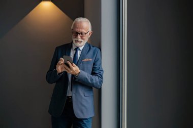 Modern ofiste cep telefonu kullanan kıdemli işadamı. Kendinden emin üst düzey yönetici, girişimci, ofisinde duran lider..