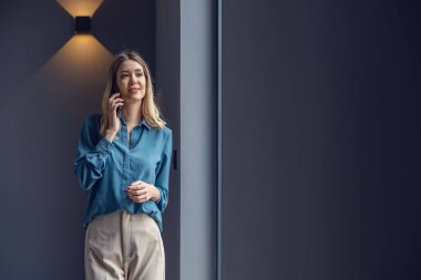 Ofisinde akıllı telefon kullanan genç bir iş kadını. Modern ofisinde duruyor..