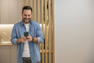 Genç serbest çalışan gülümsüyor, modern bir evde çalışıyor. İç işlerinde çalışan gülümseyen bir işadamı. Akıllı telefon kullanıyor..