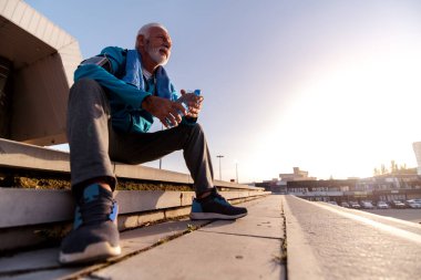 Şehirdeki antrenmandan sonra kıdemli adam dinleniyor. Fitness, spor ve sağlıklı yaşam tarzı kavramı.