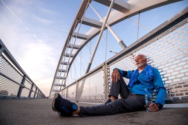 Kıdemli adam dışarıda idmandan sonra dinleniyor ve su içiyor. Fitness, spor ve sağlıklı yaşam tarzı.