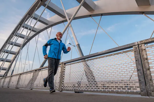 Happy senior man jogging outdoors at the bridge. Concept of healthy lifestyle.
