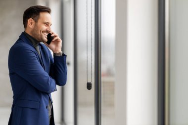 İş yerinde cep telefonu olan genç bir işadamı. Takım elbiseli bir adam ofisteki iş yerinde akıllı bir telefon tutuyor..