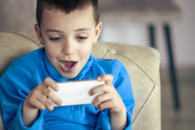 Akıllı telefonda oyun oynayan sevimli küçük çocuk. Oturma odasındaki kanepede oturan ve telefonu kullanan sevimli çocuk.. 