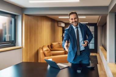 Modern ofisteki masasında çalışan bir iş adamı. Genç, gülümseyen, takım elbiseli, dizüstü bilgisayarla çalışan bir girişimci.. 