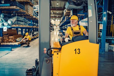 İş yerinde elektrikli forklift kullanan kıdemli işçi. Ticarette siparişlerin taşınması ve işletilmesi.