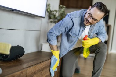 Sarı lastik eldivenli genç adam sprey ve giysi kullanarak toz temizliyor. Ev işi, temizlik ve insanlar konsepti..