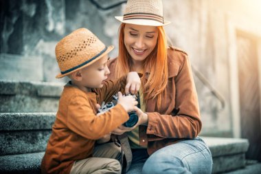 Dışarıda kamerasını kullanan güzel bir bayan fotoğrafçı. Küçük oğluna kameranın nasıl kullanılacağını öğretiyor..