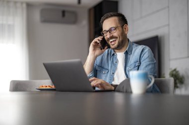 Genç serbest yazar gülümsüyor, dizüstü bilgisayarını güzel, modern bir evde kullanıyor. Ev bilgisayarında çalışan güler yüzlü bir iş adamı..
