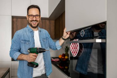 Marangoz mutfak montajını tamamlıyor. Adam mutfağa elektrikli tornavida kullanıyor. İnşaat, bakım ve onarım konsepti..