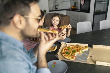 Anne, baba ve kız mutfakta pizza yiyorlar. İnsanlar, yiyecek ve içecek konsepti.