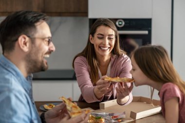 Anne, baba ve kız mutfakta pizza yiyorlar. İnsanlar, yiyecek ve içecek konsepti.