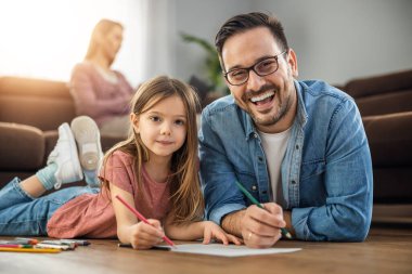 Genç baba ve küçük kızı birlikte oynuyorlar. Renkli kalemlerle çiziyorlar..