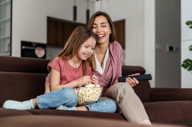 Anne ve kızı oturma odasında televizyon izliyorlar. Birlikte güzel vakit geçiriyorlar..
