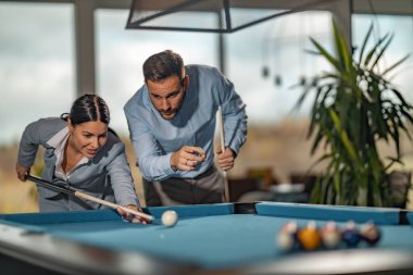 İş arkadaşları işten sonra ofiste bilardo oynuyorlar. Kadın masadaki top piramidini kırmaya hazırlanıyor..
